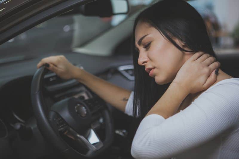 female driver rubbing her neck after car crash