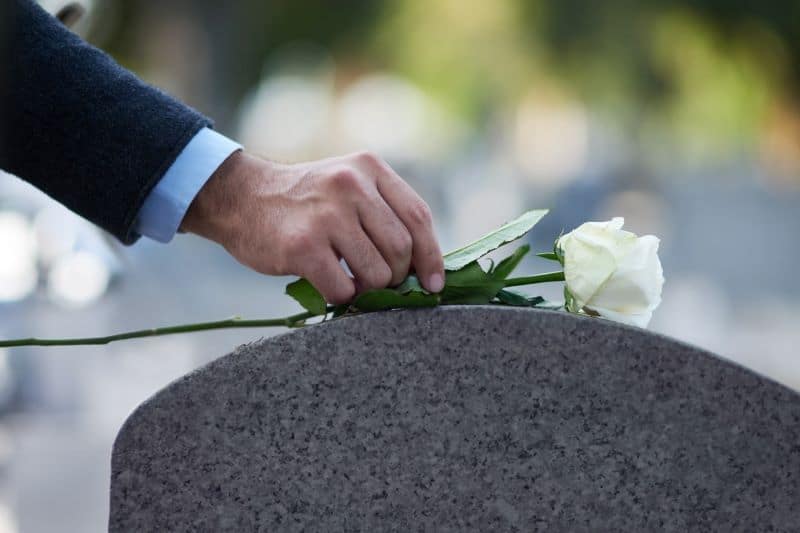 man leaving a rose on his wife's grave