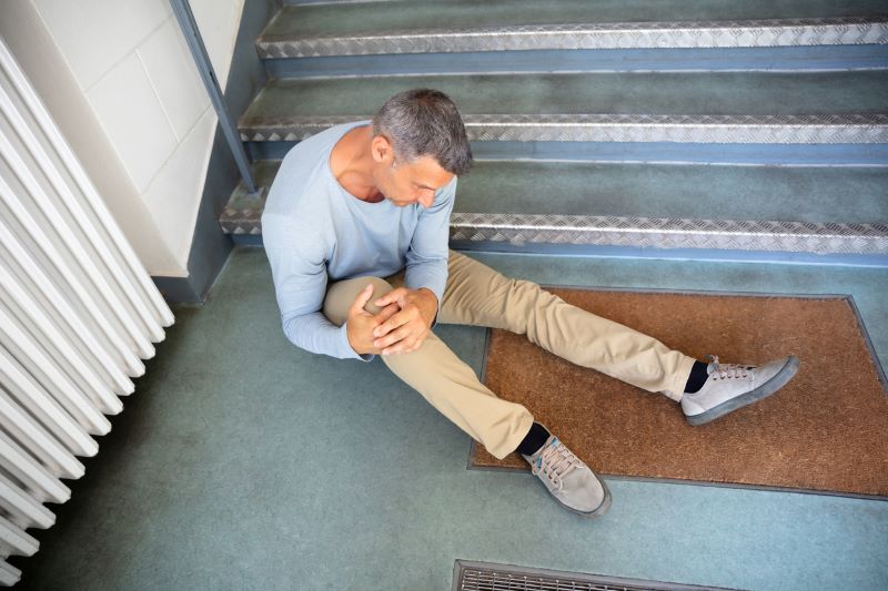 man sitting at the bottom of the staircase after falling and injuring his leg