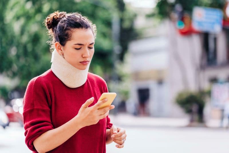 woman looking at her cell phone with a neck brace on due to a serious neck injury